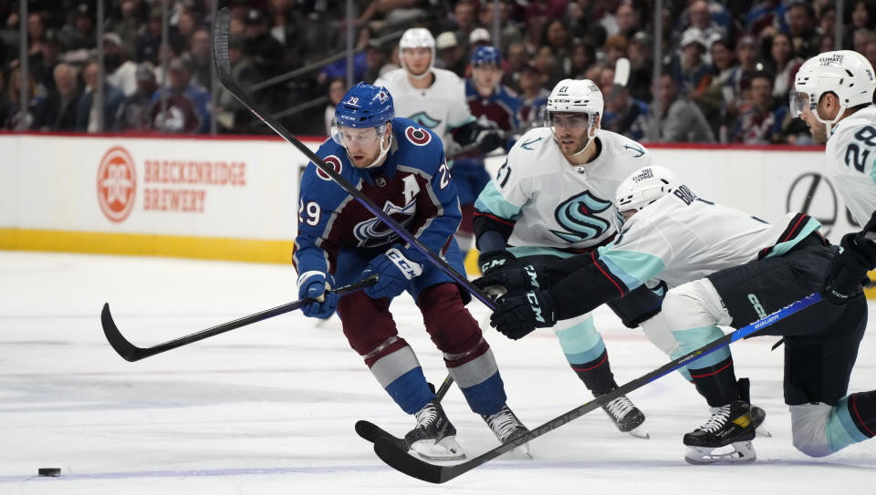 Colorado Avalanche center Nathan MacKinnon, left, pursues the puck with Seattle Kraken center Alex Wennberg (21) and defenseman Will Borgen during the first period of an NHL hockey game Friday, Oct. 21, 2022, in Denver. (AP Photo/David Zalubowski)