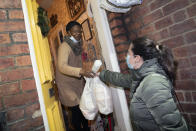 Volunteer Maria Martinez, right, hands bags of West Indian meals to Bridgette Toussaint, prepared by members of the Preston Windrush Covid Response team, in Preston, England, Friday Feb. 19, 2021. Once a week chief coordinator Glenda Andrew and her team distribute meals to people in Preston and surrounding communities in northwestern England that have recorded some of the U.K.’s highest coronavirus infection rates. The meal program grew out of Andrew’s work with Preston Windrush Generation & Descendants, a group organized to fight for the rights of early immigrants from the Caribbean and other former British colonies who found themselves threatened with deportation in recent years. (AP Photo/Jon Super)