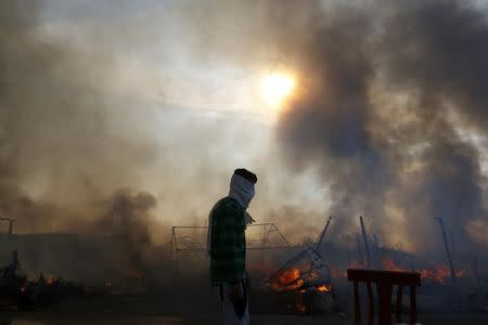 A migrant is seen in silhouette as smoke fills the sky from burning makeshift shelters in the "Jungle" on the third day of their evacuation and transfer to reception centers in France, as part of the dismantlement of the camp in Calais, France, October 26, 2016. REUTERS/Pascal Rossignol