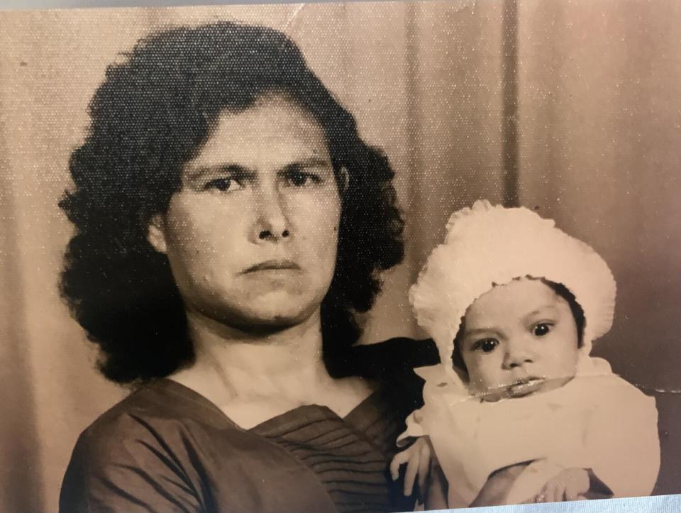 A woman with a serious expression holds an infant