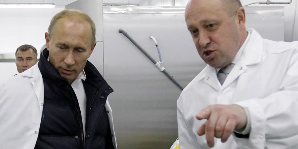 Putin and Prigozhin in white coats, with the latter pointing at something off-camera