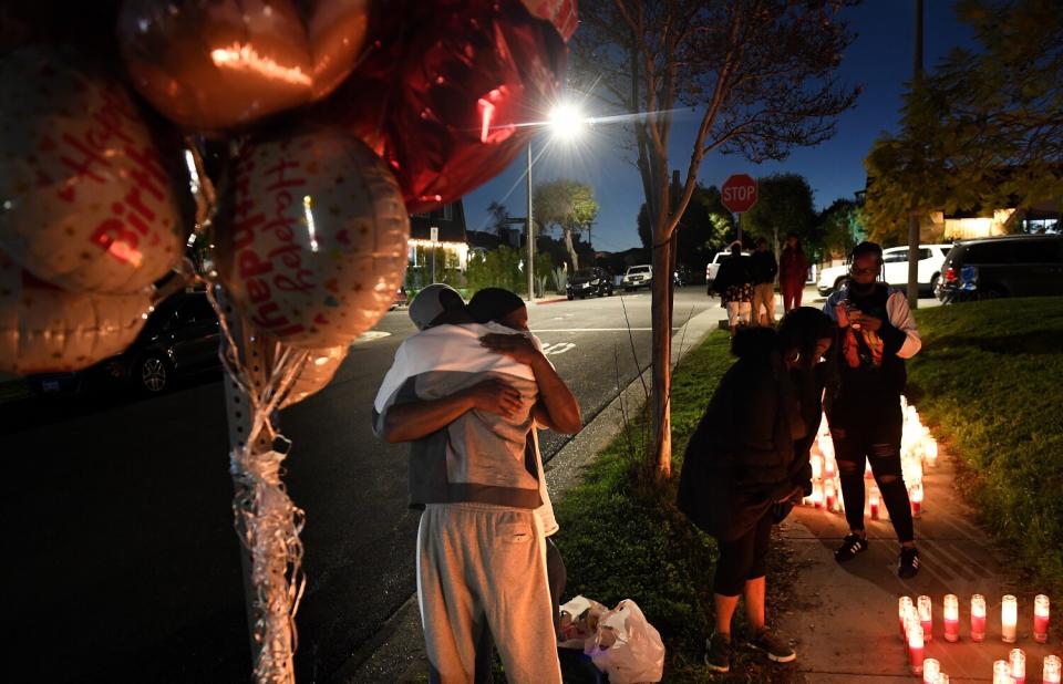 Two people hug on a sidewalk lined with balloons and lighted candles at night