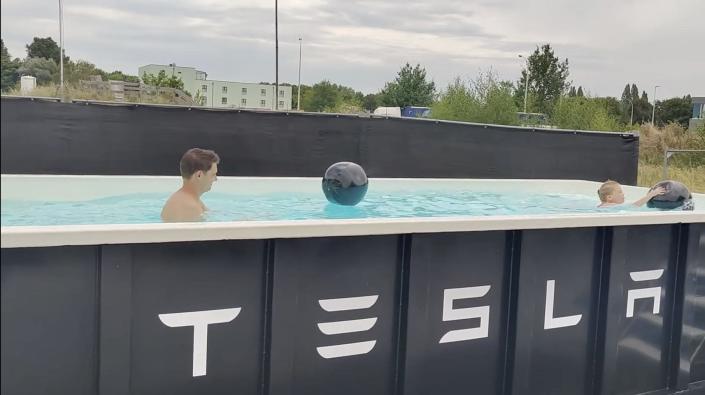 a man and a little girl swim in a black metal pool that has tesla written on the front of it