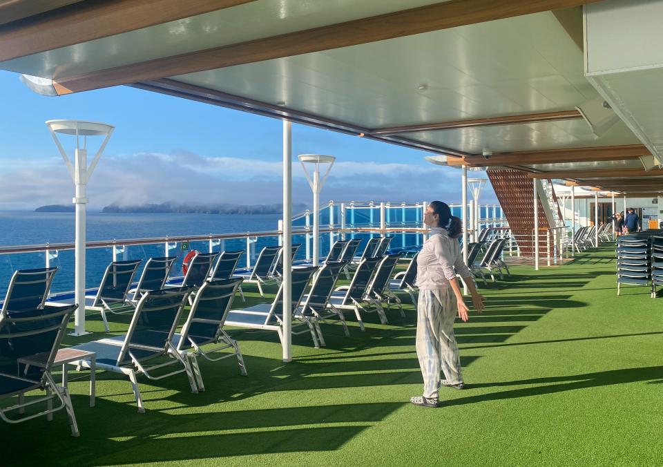 A woman stretching on a cruise deck facing the sea.