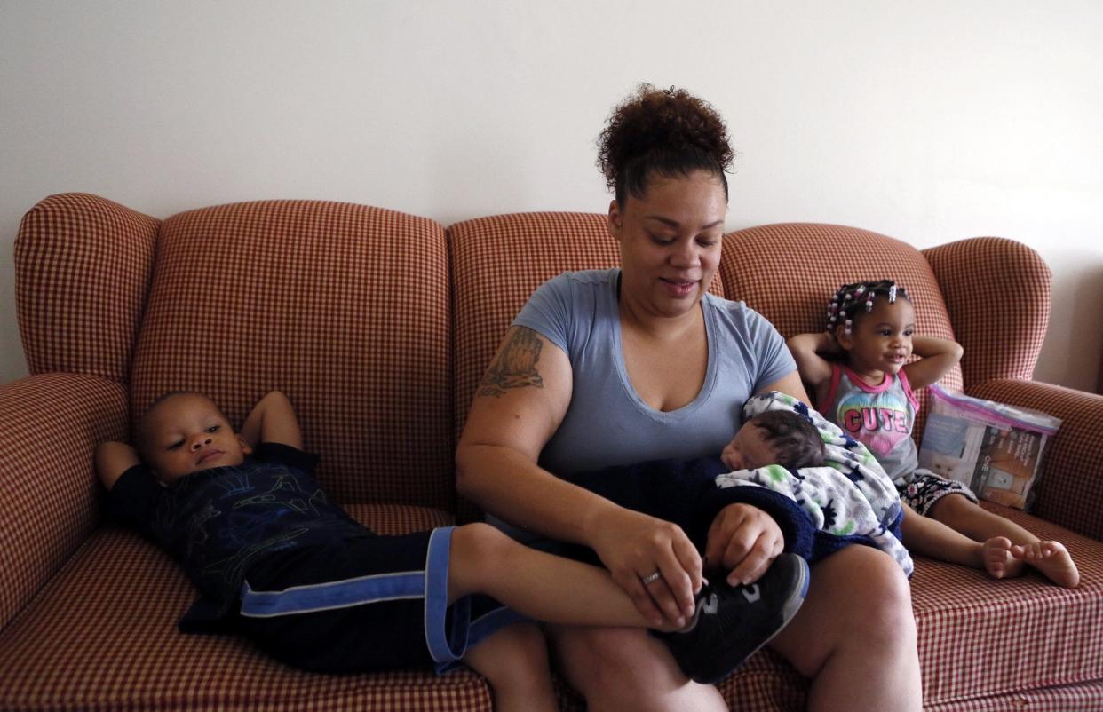 Michel'e Miller holds her new baby while she ties the shoes of her son, as her daughter stretches out on the couch in July 2019. She was enrolled in a program that seeks to reduce infant morality by helping homeless pregnant women and new moms find stable housing.[Eric Albrecht/Dispatch]