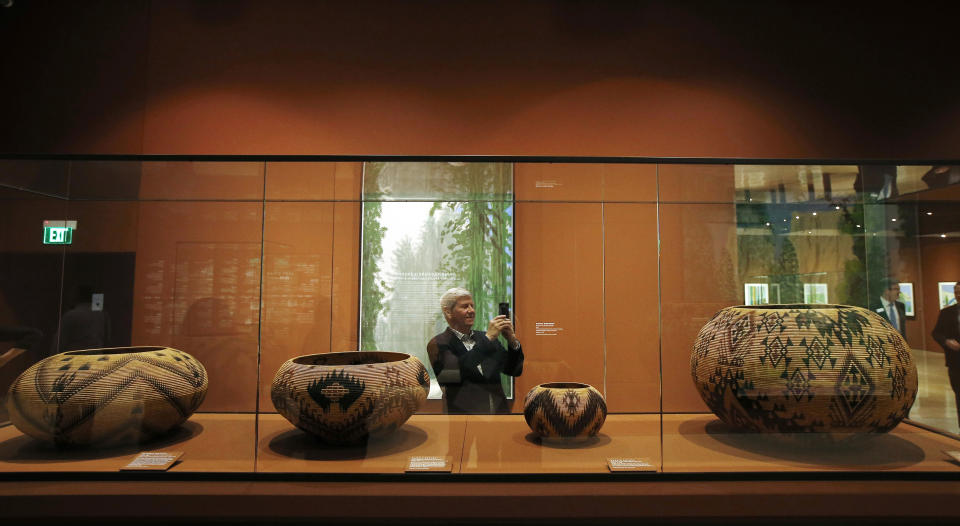 In this Wednesday, Oct. 23, 2019, photo, Richard Benefield, former executive director of the David Hockney Foundation, takes a photo inside the exhibit of Hockney's Yosemite artistic work, background, along with baskets from weavers from the Miwok and Mono Lake Paiute tribes on display at the Heard Museum in Phoenix. "David Hockney's Yosemite and Masters of California Basketry" exhibition opens Monday. (AP Photo/Ross D. Franklin)