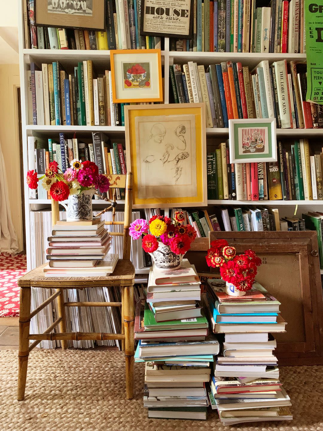 piles of books on the floor and on a chair next to a packed bookshelf