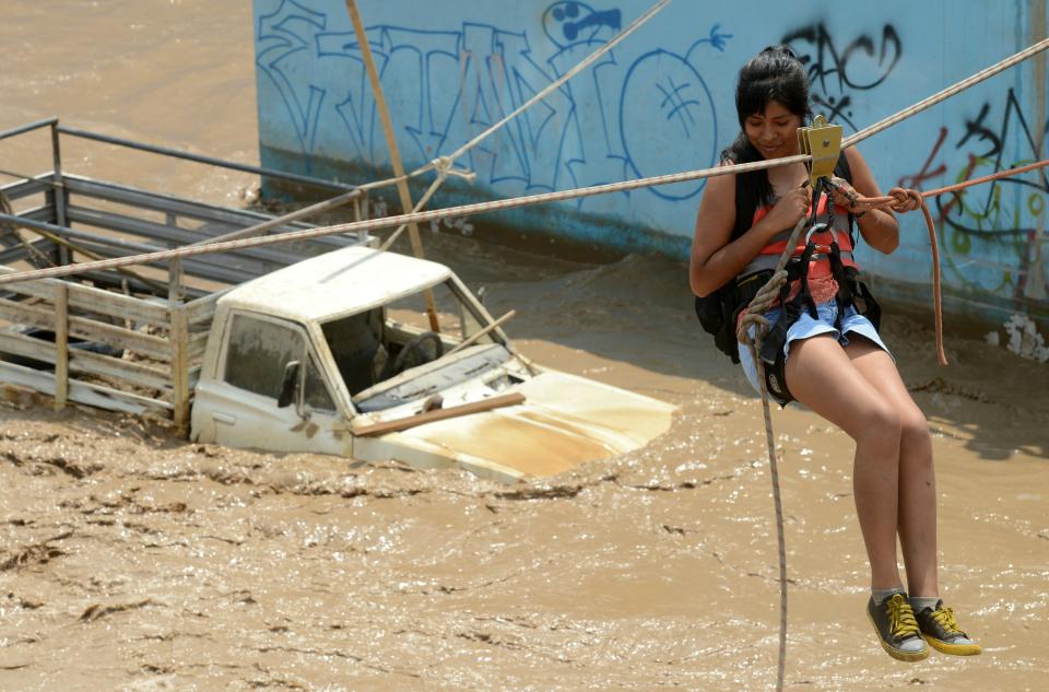 Residents of the Huachipa populous district, east of Lima, Peru, are helped on March 17, 2017, by police and firemen rescue teams to cross over flash floods hitting their neighborhood and isolating its residents.