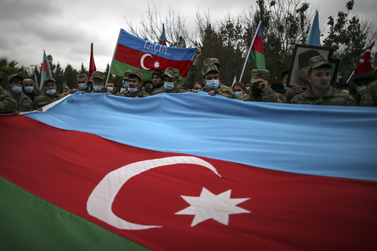 Azerbaijani soldiers hold a huge national flag as they celebrate the transfer of the Lachin region to Azerbaijan's control, as part of a peace deal that required Armenian forces to cede the Azerbaijani territories they held outside Nagorno-Karabakh, in Aghjabadi, Azerbaijan, Tuesday, Dec. 1, 2020. Azerbaijan has completed the return of territory ceded by Armenia under a Russia-brokered peace deal that ended six weeks of fierce fighting over Nagorno-Karabakh. Azerbaijani President Ilham Aliyev hailed the restoration of control over the Lachin region and other territories as a historic achievement. (AP Photo/Emrah Gurel