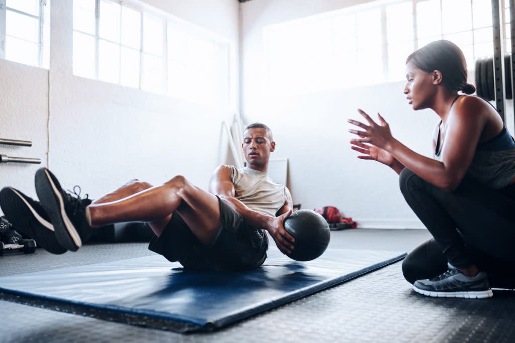 A personal trainer works with a client as they do crunches with a medicine ball. 