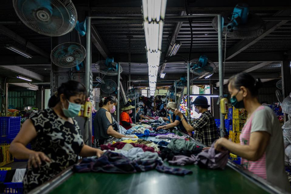 Women surround a conveyor belt of clothing they are sorting.