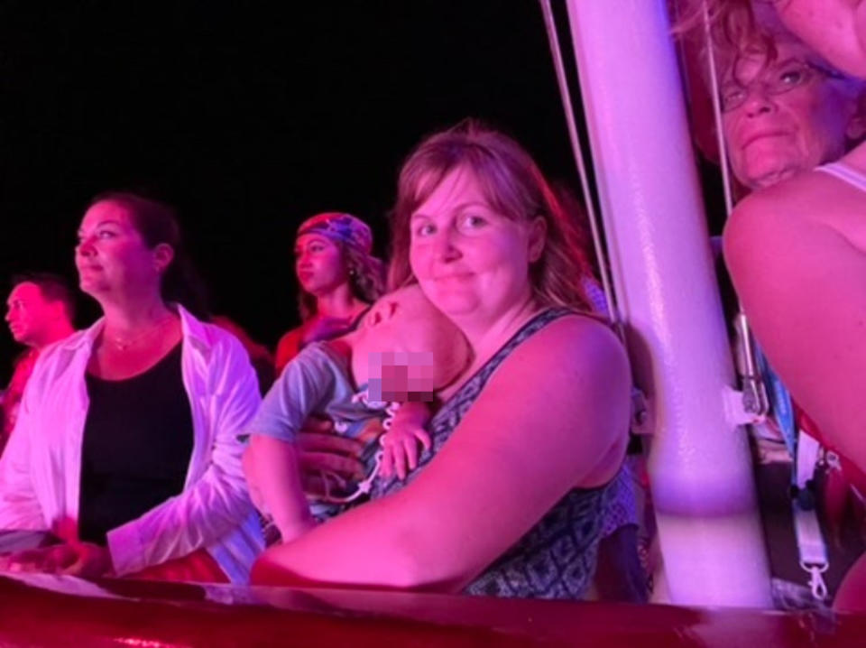 A mother holds her sleeping child closely among a group of people at an event