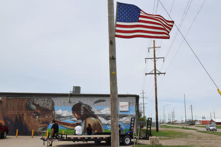 People sit in front of a mural depicting a buffalo and a Native American man along the main road on the Cheyenne River Reservation in Eagle Butte, South Dakota, U.S., May 28, 2018. REUTERS/Stephanie Keith