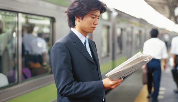 Businessman reading newspaper on railway station, side view