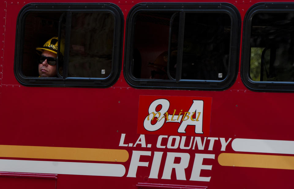 A Los Angeles County Firefighter looks up at the Palisades Fire before gearing up to fight the flames in the Pacific Palisades area of Los Angeles, Monday, Oct. 21, 2019. The blaze broke out Monday morning in a coastal canyon of the affluent Pacific Palisades neighborhood. The flames quickly churned uphill through dry brush as helicopters made water drops to keep it from reaching large houses at the top of a bluff. Firefighters in backyards are using water hoses to protect structures. The cause is unknown. (AP Photo/Christian Monterrosa)