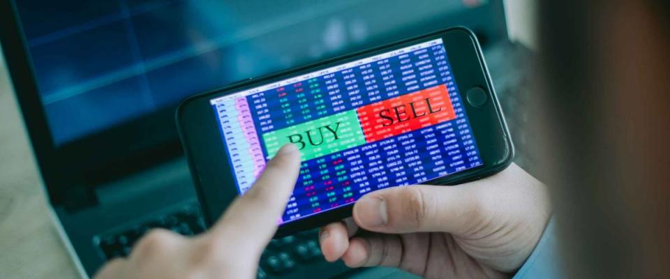 Hand of trader holding mobile phone touch screen showing buy and sell in Stock market order and blurred bakcground of laptop show financial chart, business trading concept