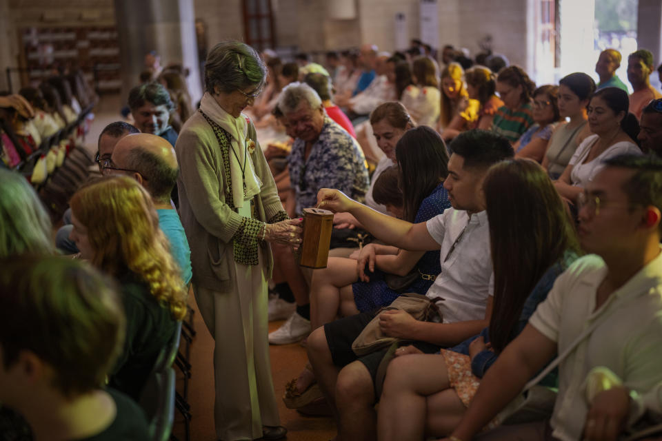 A volunteer holds a box while taking donations from the faithful during a Mass in the Sagrada Familia basilica in Barcelona, Spain, Sunday, July 9, 2023. With tourism reaching or surpassing pre-pandemic levels across Southern Europe this summer, iconic sacred sites struggle to find ways to accommodate both the faithful who come to pray and millions of increasingly secular visitors attracted by art and architecture. (AP Photo/Emilio Morenatti)