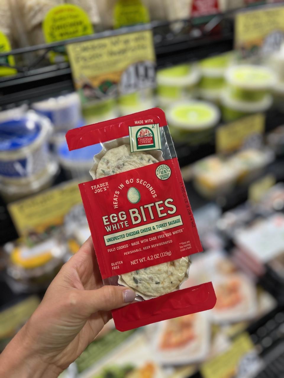 Hand holding a package of Trader Joe's Egg White Bites with cheese & turkey sausage in a grocery store