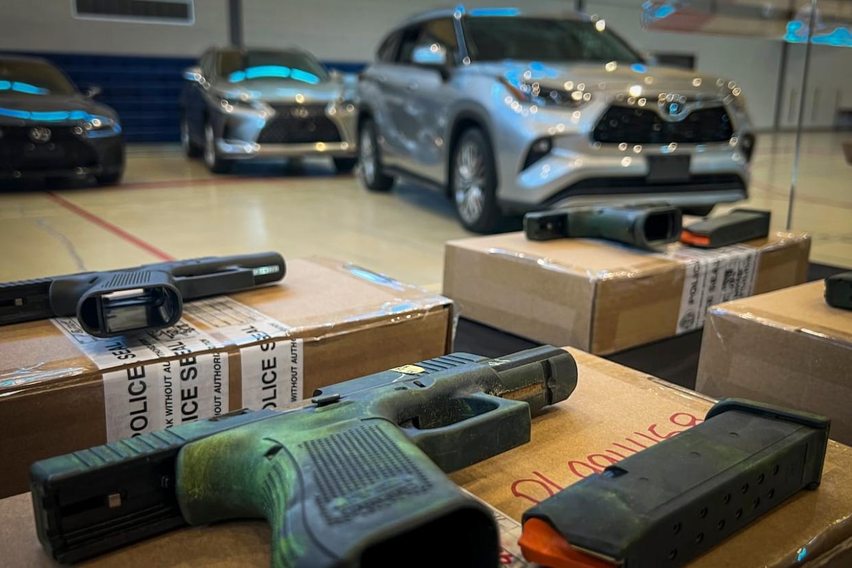 Handguns are pictured near recovered stolen cars during a Toronto Police Service press conference in Toronto on Wednesday, March 27, 2024. (Greg Bruce/CBC - image credit)