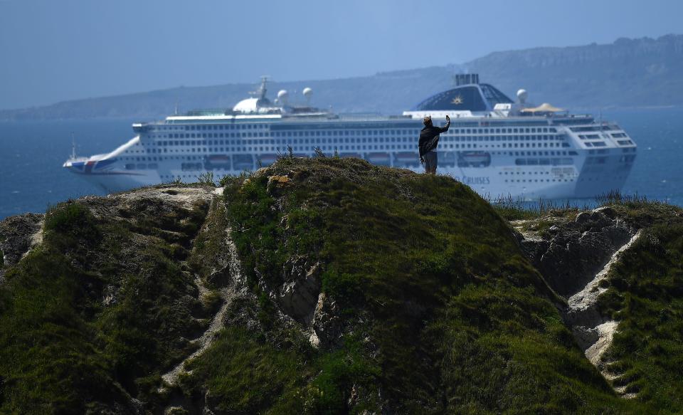 A man takes a selfie photo atop the Durdle Door rock, as a Cruise ship is seen in the sea beyond, near West Lulworth on the south coast of England on May 24, 2020. -