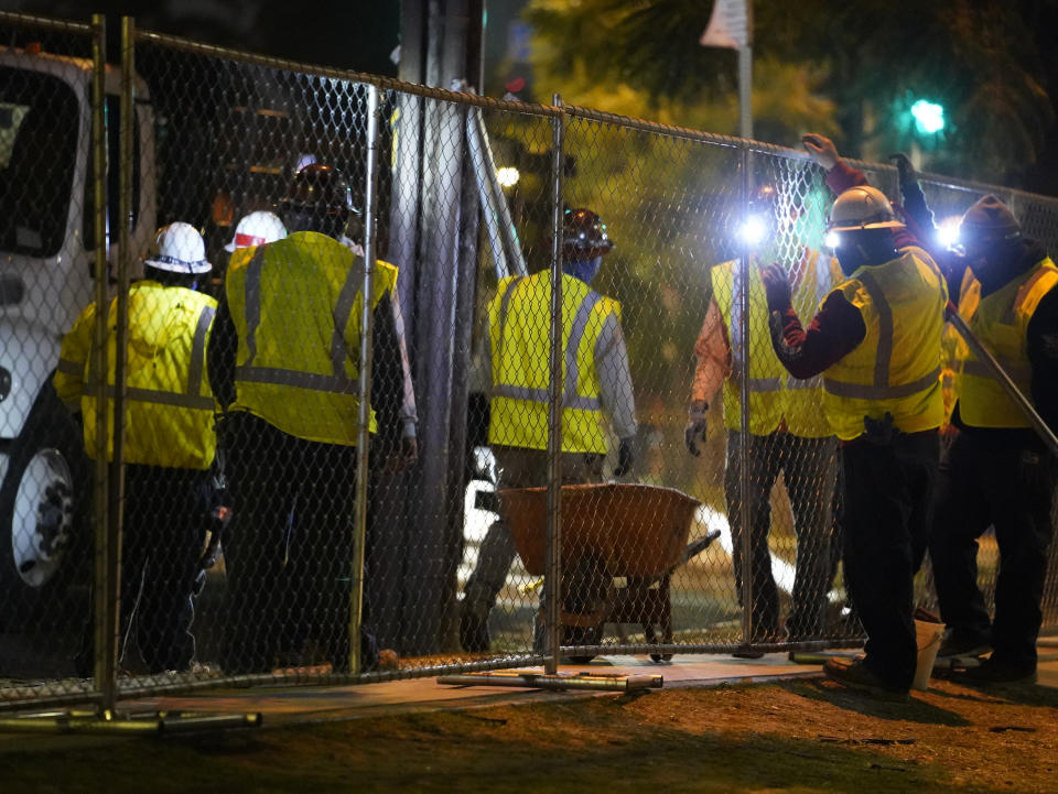 Los Angeles city contractors install a temporary fence around Echo Park Lake's perimeter in Los Angeles early Thursday, March 25, 2021. Los Angeles Police officers sweep managed to corral demonstrators gathered Wednesday to protest the planned closure of a Los Angeles park that would displace a large homeless encampment that has grown throughout the coronavirus pandemic. The park will be closed for repairs.(AP Photo/Damian Dovarganes)