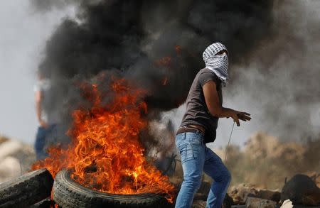 A masked Palestinian stands next to a burning tyre during clashes with Israeli troops in the West Bank village of Khobar near Ramallah July 22, 2017. REUTERS/Mohamad Torokman