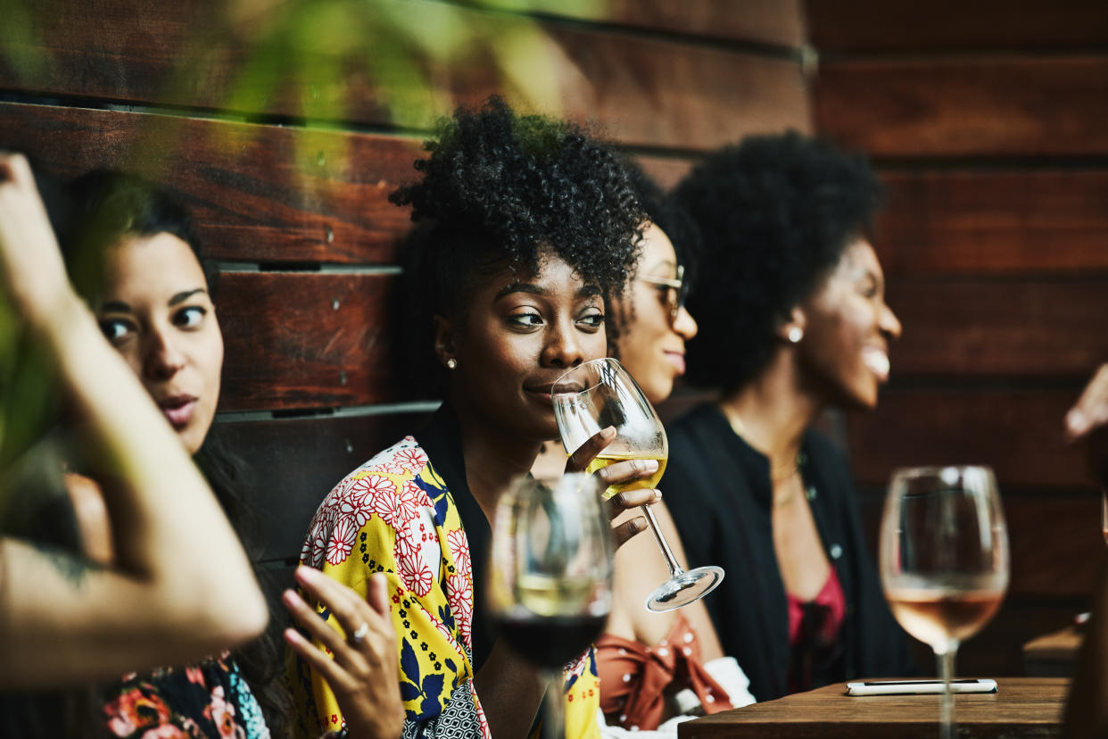 A woman seated at a restaurant table holds a glass of wine as others around her talk amongst themselves.