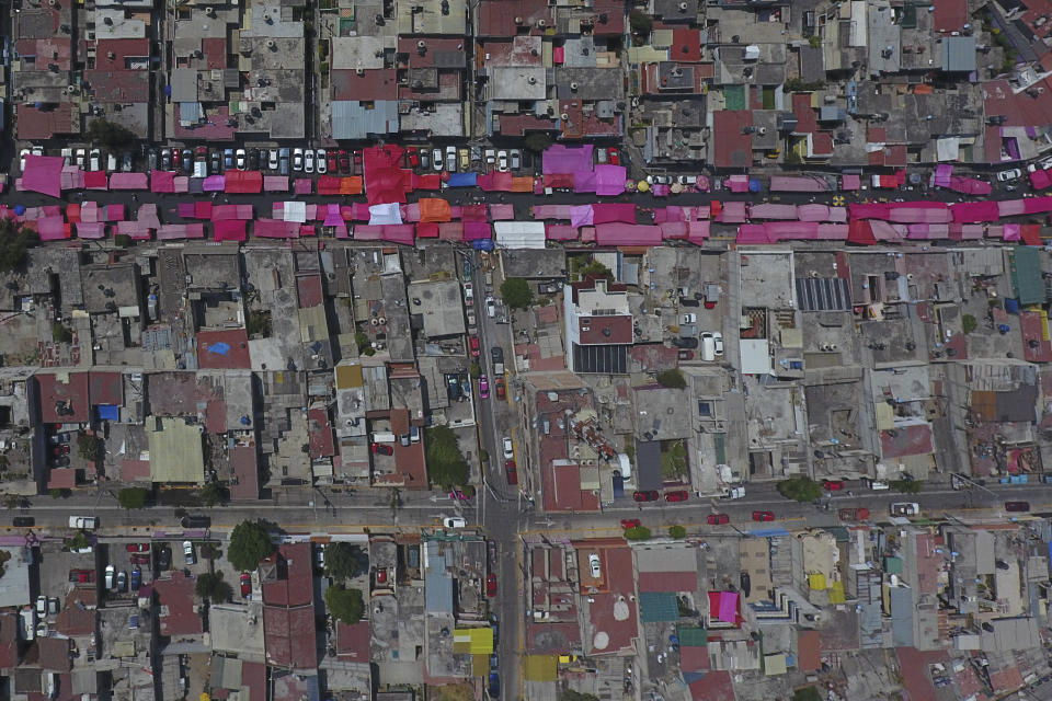 Stalls shielded from the sun with pink awnings line a road during a reduced, but still active weekly street market in northern Mexico City, Sunday, March 29, 2020, as many people stay home amid the spread of the new coronavirus. (AP Photo/Rebecca Blackwell)