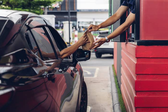 A person in a car receives a paper bag from a worker at a drive-through window