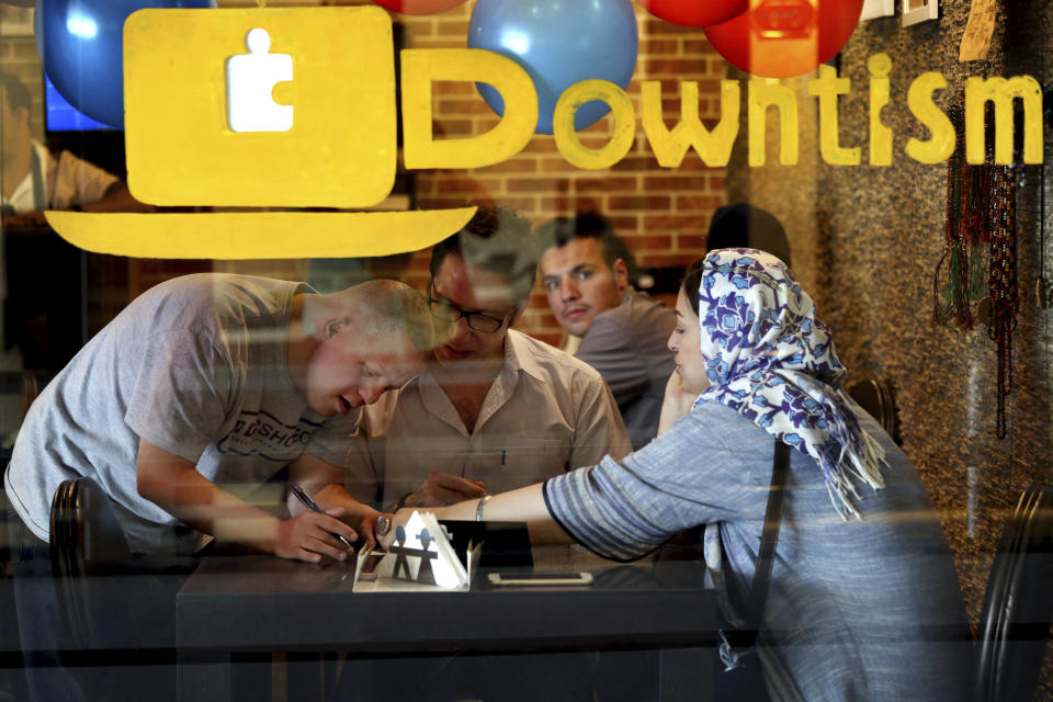 In this Monday, Aug. 6, 2018 photo, cafe staffer Ali Bakhti, with down syndrome, left, takes order in Downtism Cafe in Tehran, Iran. The popular cafe in Tehran’s bustling Vanak Square, whose name combines “Down” with “autism,” is entirely run by people with Down syndrome or autism. More than just providing meaningful work, the cafe is helping break down barriers by highlighting how capable people with disabilities are. (AP Photo/Ebrahim Noroozi)