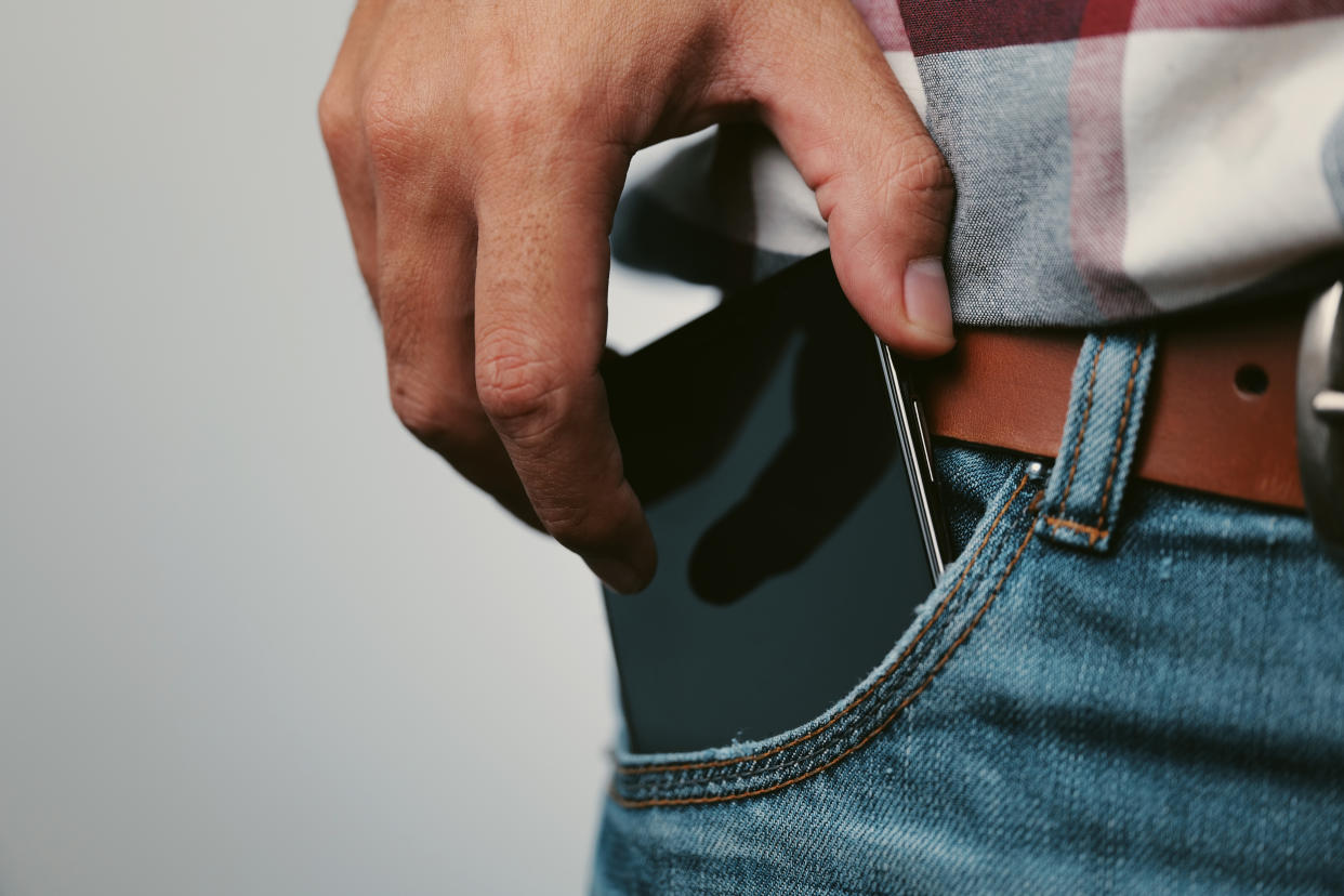 A man puts a cellphone in the front pocket of his jeans.