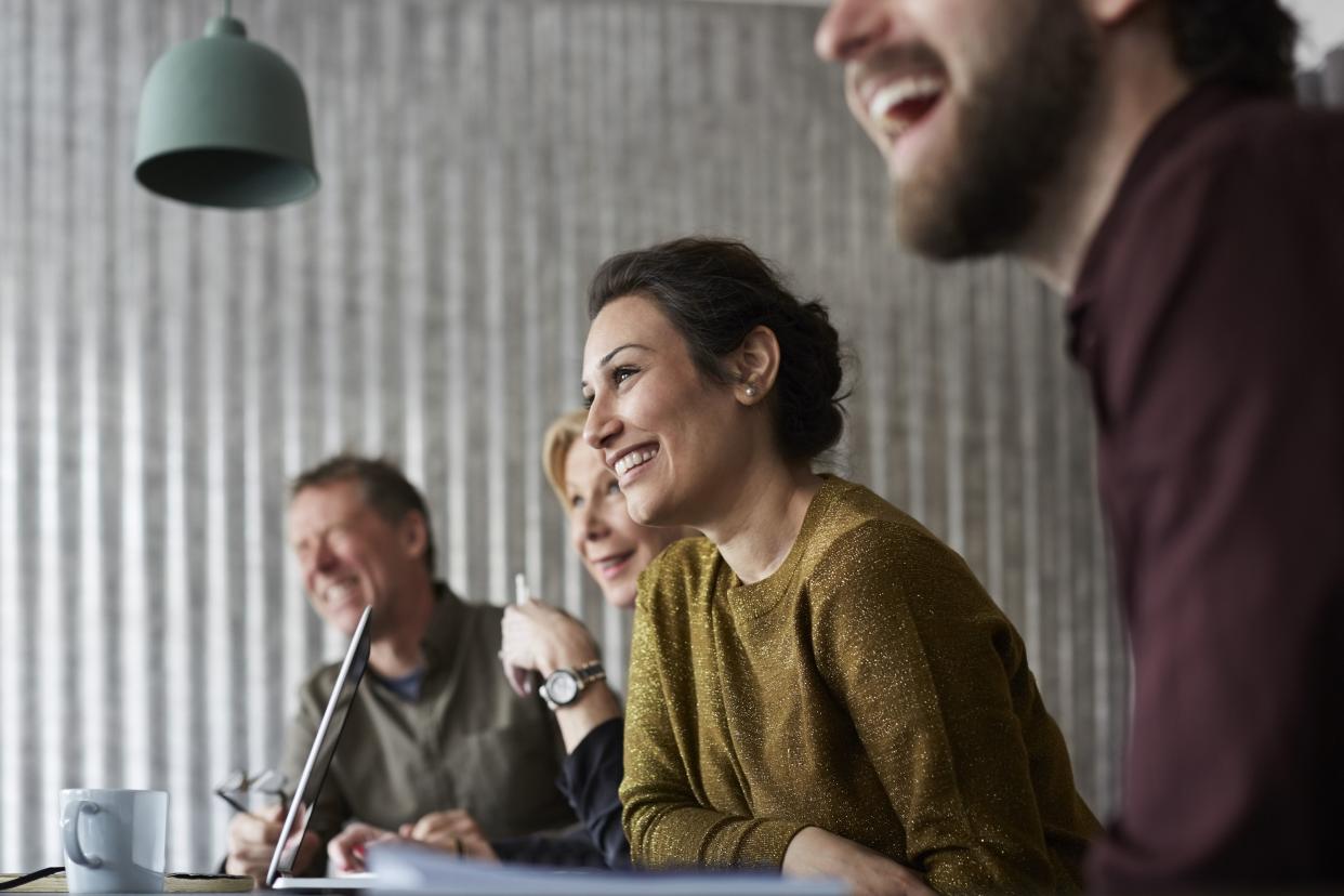 cheerful creative business colleagues sitting at conference table while looking away in board room