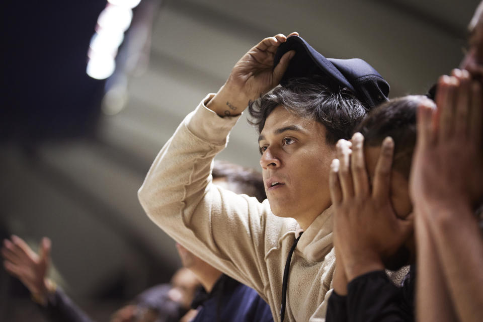 A person is adjusting a baseball cap on their head, surrounded by others in a similar pose