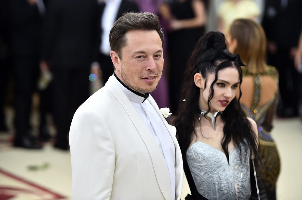 Elon Musk in a white tuxedo and a person in a silver outfit with structured shoulders and a choker at an event