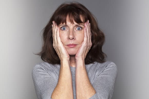 A woman clasps her palms to her cheeks.