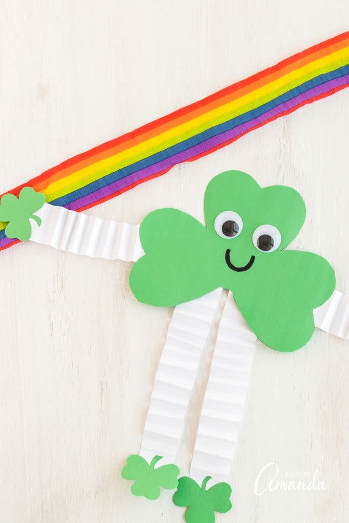 smiling green paper shamrock with googly eyes and arms and legs made out of white construction paper