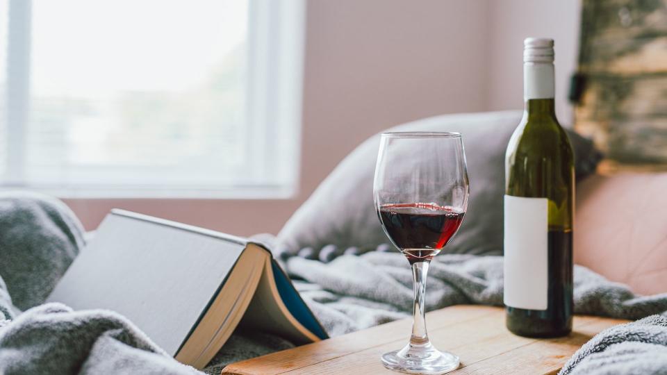 Shot of a glass of red wine and a book on the bed at home