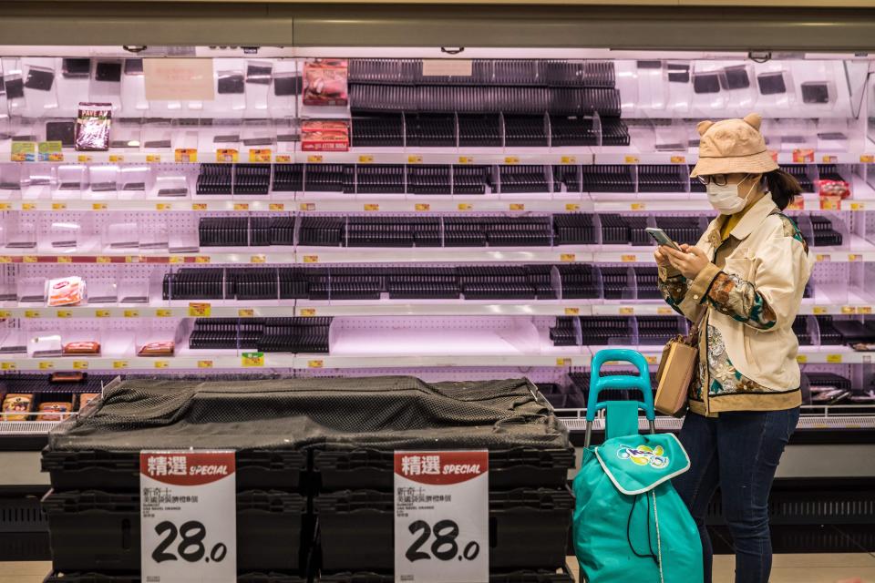 A woman looks at her phone in front of empty shelves at a supermarket in Hong Kong on March 1, 2022,