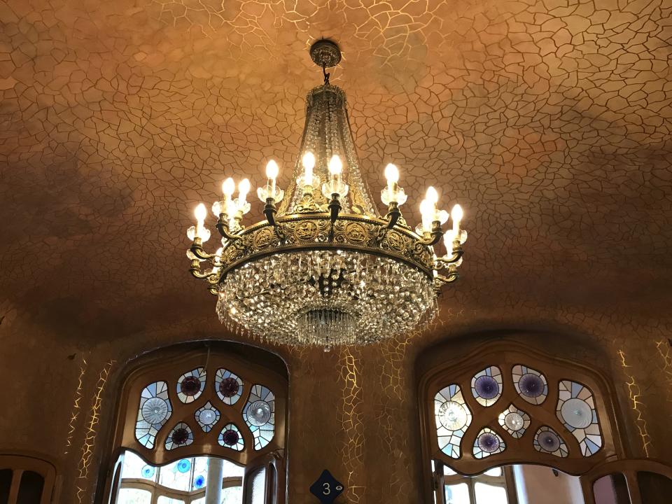 This Oct. 12, 2019 photo shows a chandelier hanging from a decorative roof near stained-glass doorways in Anton Gaudí’s Casa Batlló in Barcelona, Spain. (Courtney Bonnell via AP)