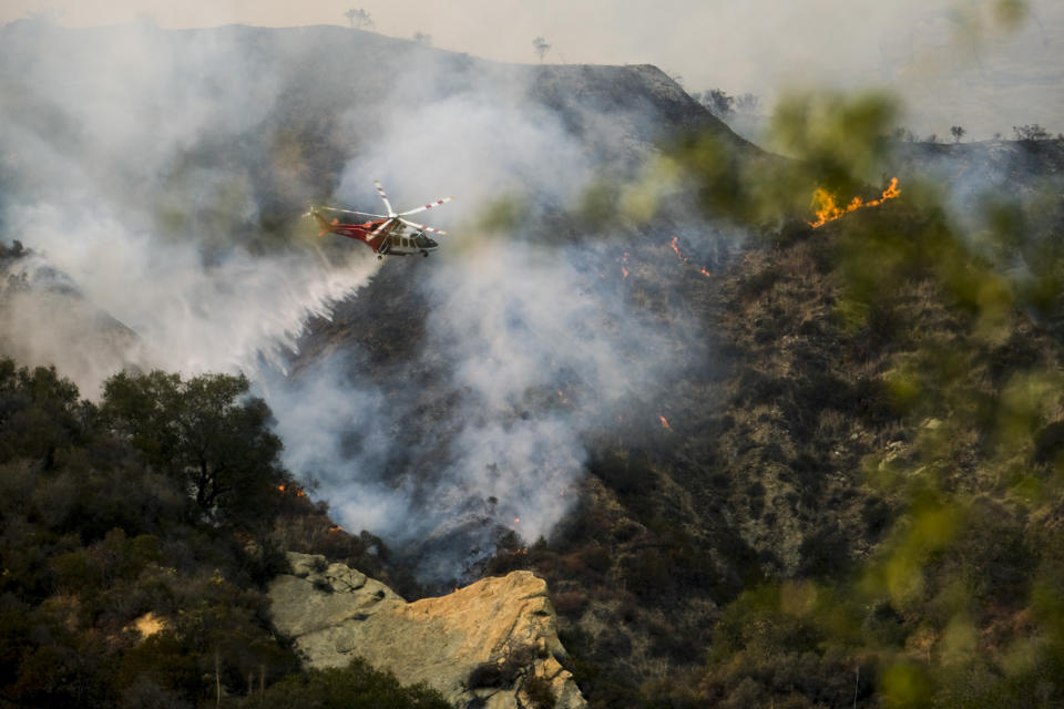 A firefighting helicopter drops water on a brush fire scorching at least 100 acres in the Pacific Palisades area of Los Angeles Saturday, May 15, 2021. (AP Photo/Ringo H.W. Chiu)