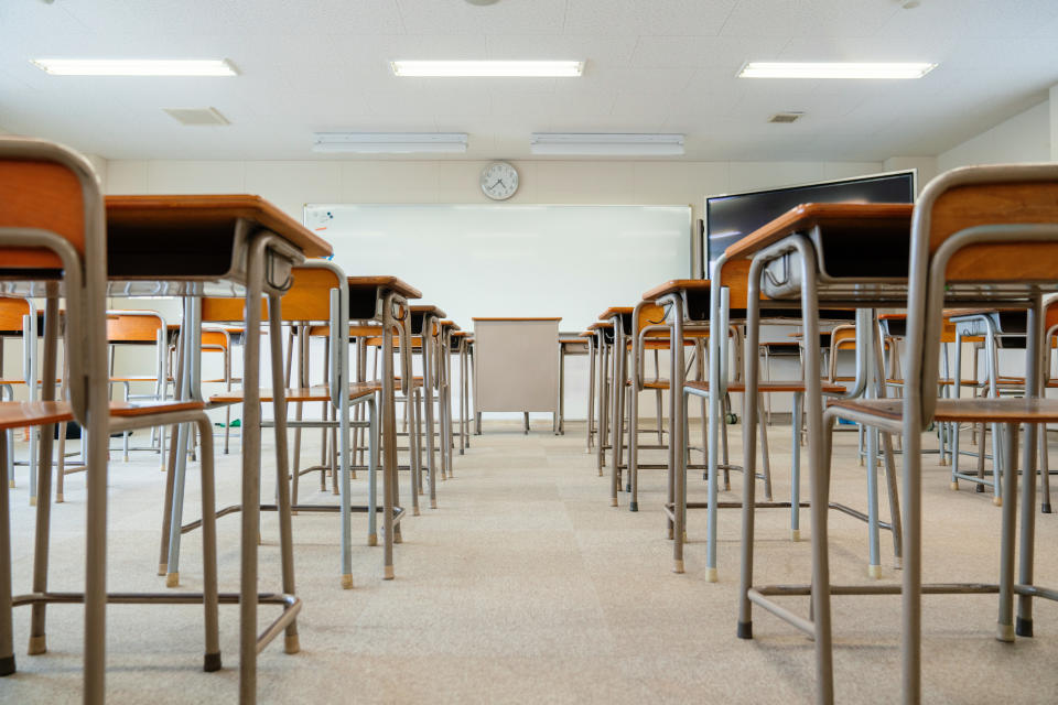 Empty classroom with rows of desks and chairs facing a whiteboard and clock