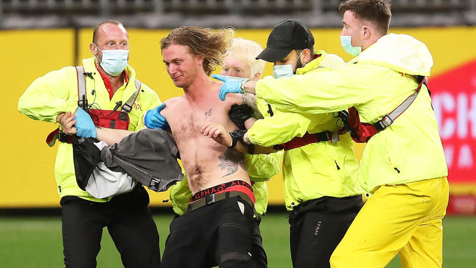 Security is pictured escorting a pitch invader off the field at Optus Stadium during the round 7 match between Geelong and Collinngwood.