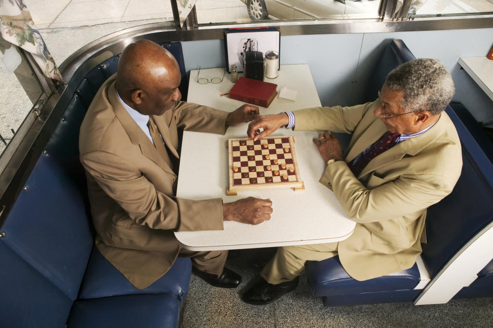 Two men wearing suits playing a game of checkers at a table in a diner booth