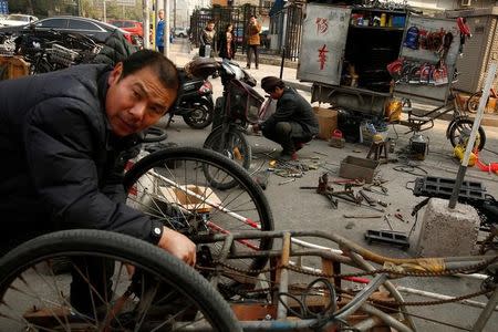 A man repairs a three-wheeled vehicle (foreground) typically used by garbage collectors at a pop-up repair shop on a pavement in Beijing, China, November 3, 2016. REUTERS/Thomas Peter/Files