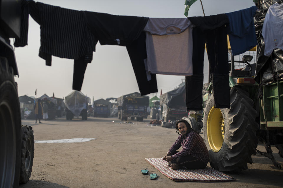 Davender Singh, 29, basks in the morning sun next to his tractor as he joins farmers protesting new laws they say will result in their exploitation by corporations, at the Delhi-Haryana state border, India, Tuesday, Dec. 1, 2020. The farmers have have hunkered down, supplied with enough food and fuel to last weeks. Prime Minister Narendra Modi's government, rattled by the growing rebellion, insists the reforms will benefit them. But the farmers aren’t yielding. (AP Photo/Altaf Qadri)