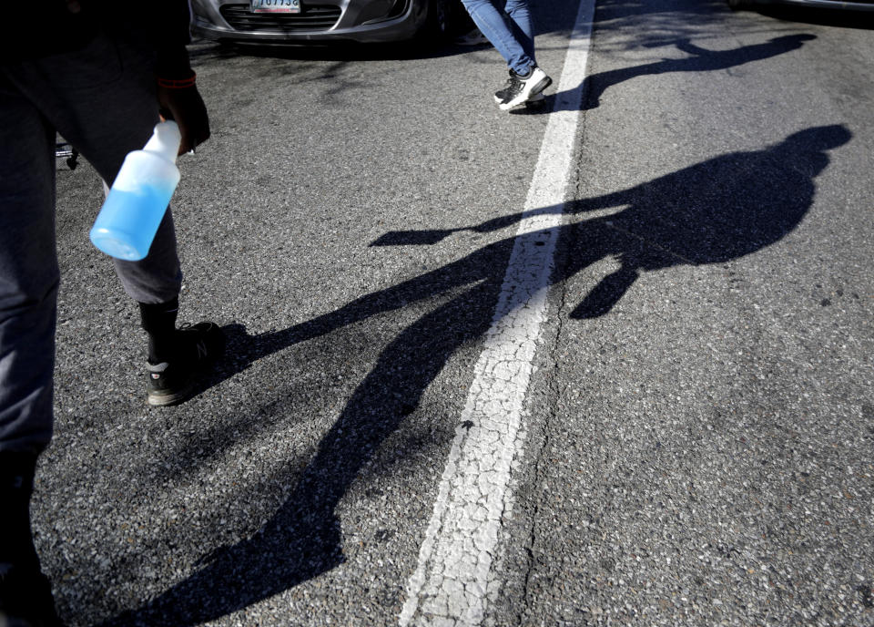 In a photo taken Thursday, Oct. 24, 2019, Jerome Holloway, left, walks with his spray bottle and squeegee in the middle of stopped traffic as he works a corner in Baltimore. A debate over Baltimore's so-called squeegee kids is reaching a crescendo as the city grapples with issues of crime and poverty and a complicated history with race relations. Officials estimate 100 squeegee kids regularly work at intersections citywide, dashing into the street as red lights hit to clean windshields in exchange for cash from drivers. (AP Photo/Julio Cortez)