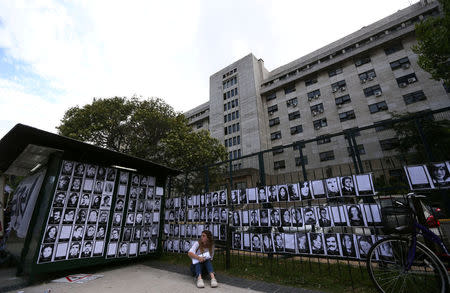 A woman sits next to portraits of people who disappeared during Argentina's military dictatorship, outside a courthouse where the sentence hearing of the five-year trial for the role of Navy officers during the 1976-1983 dictatorship is being held, in Buenos Aires, November 29, 2017. REUTERS/Marcos Brindicci