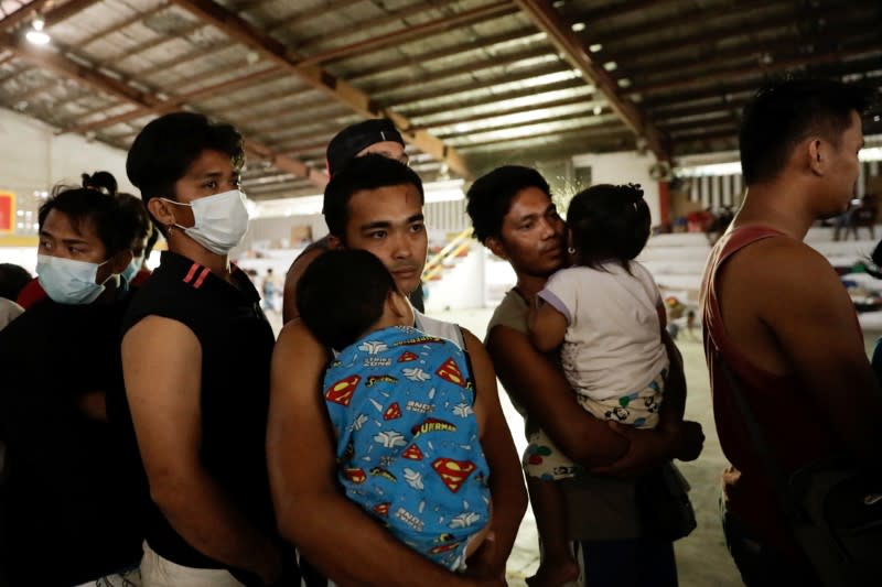 Men carrying their babies queue for food in an evacuation center for residents affected by the Taal Volcano erruption in Santo Tomas