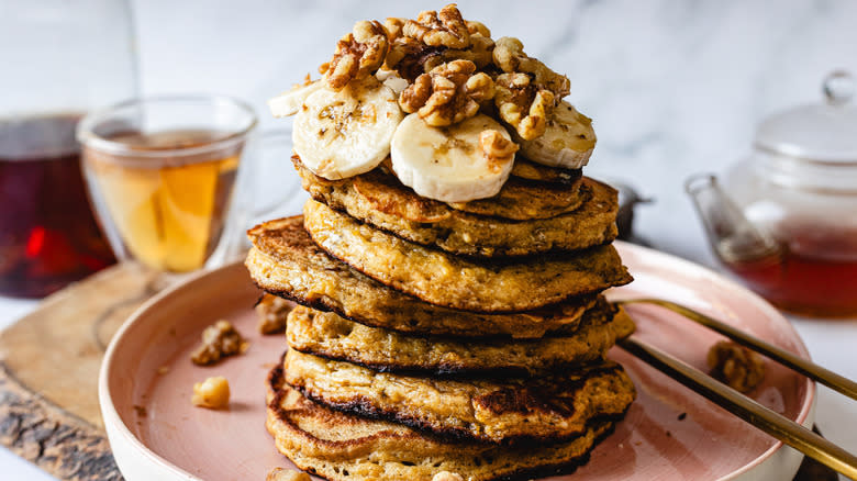 Stack of pancakes with bananas and walnuts with tea supplies in back
