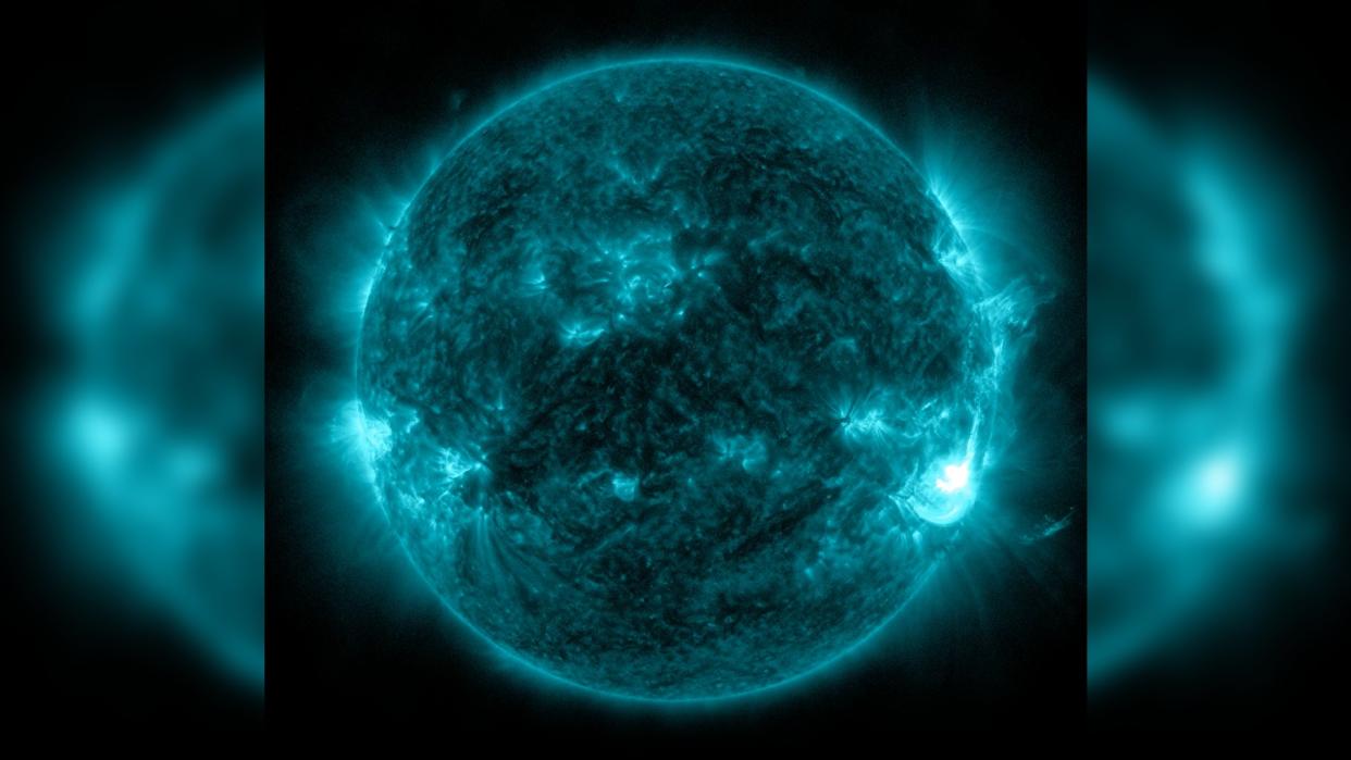  A green false-color image of the sun shows a large plume of white light exploding out of its southeastern edge. 